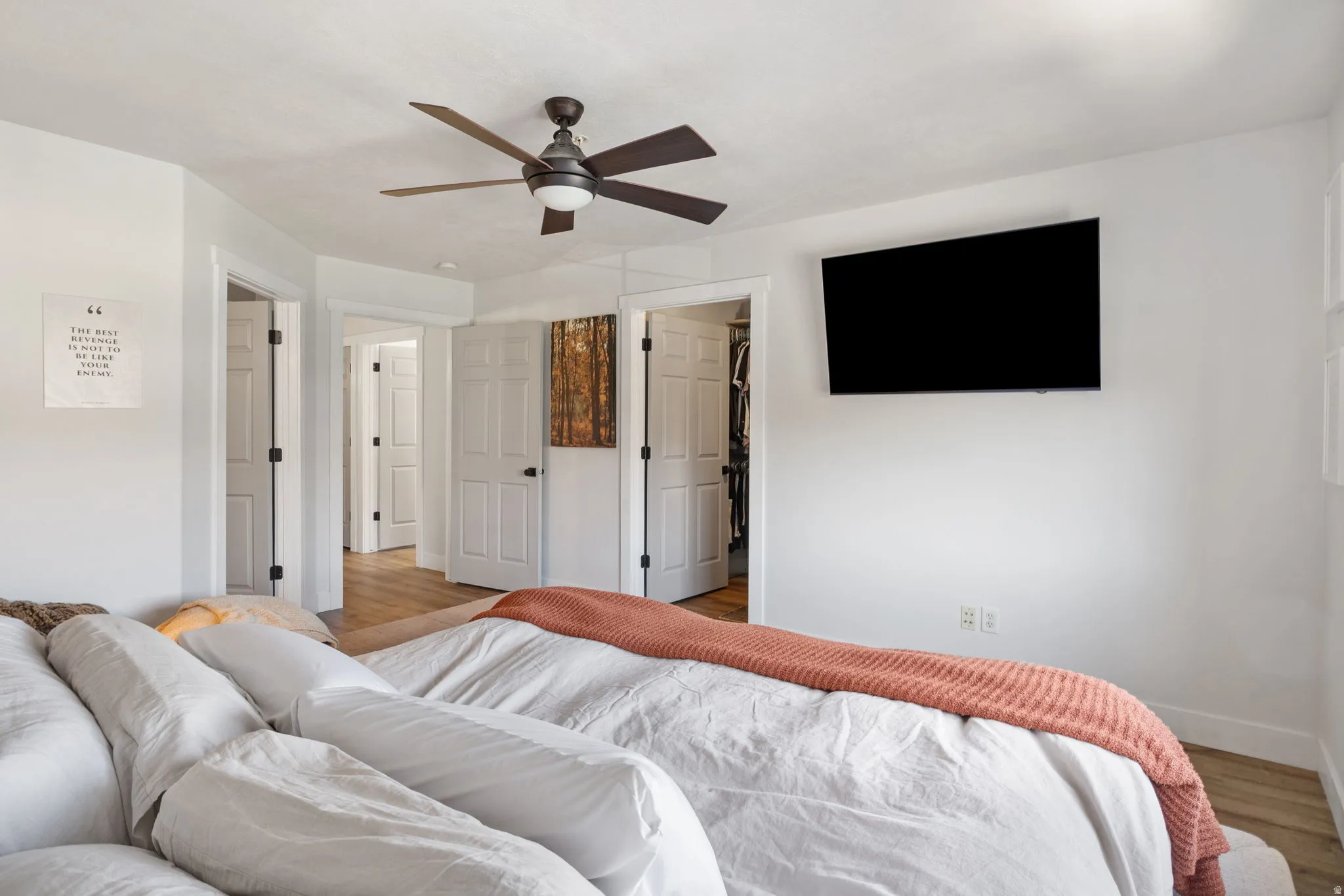 Bedroom featuring wood-finish flooring, white paneled doors, and a ceiling fan with integrated lighting
