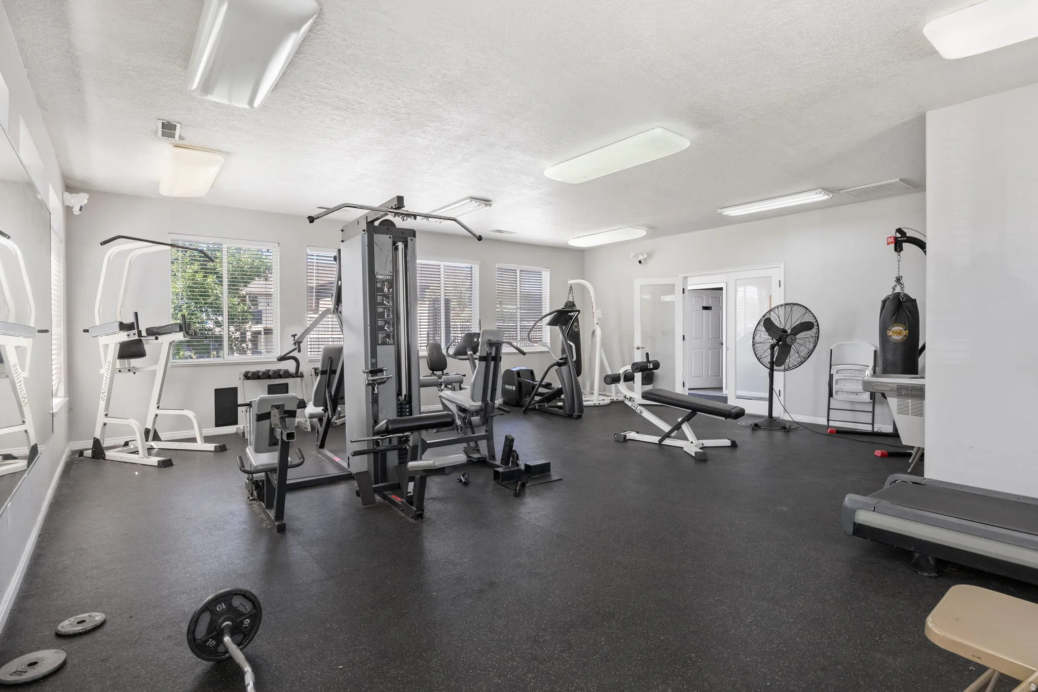 Dedicated fitness area featuring durable rubber flooring, multiple windows providing natural light, overhead fluorescent lighting, and a mirrored wall