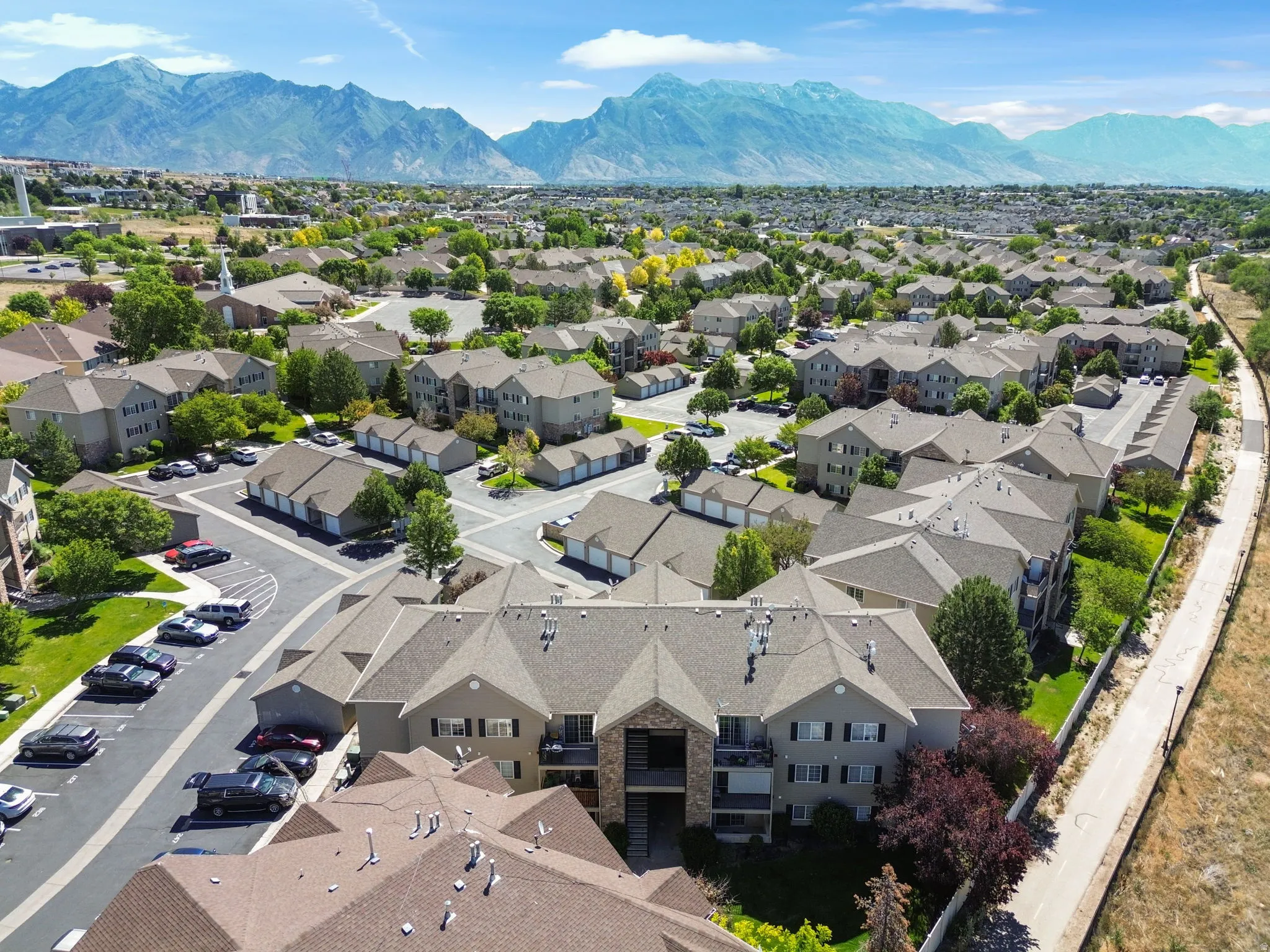 Expansive aerial showcasing a community of multi-story residential buildings with pitched roofs, surrounded by mature trees and manicured green spaces