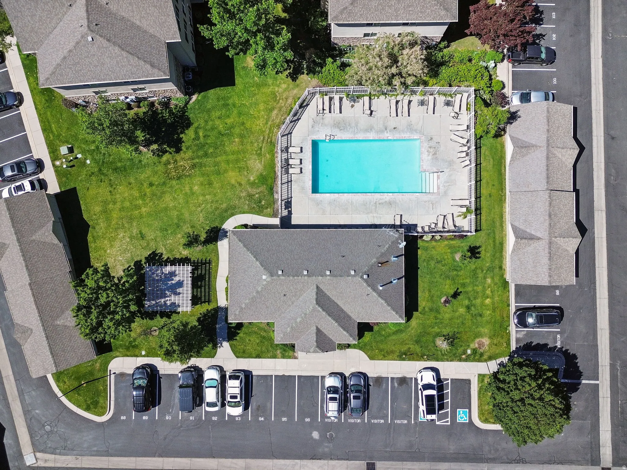 Aerial view showcasing the community pool with surrounding lounge deck, extensive green spaces, and ample surface parking