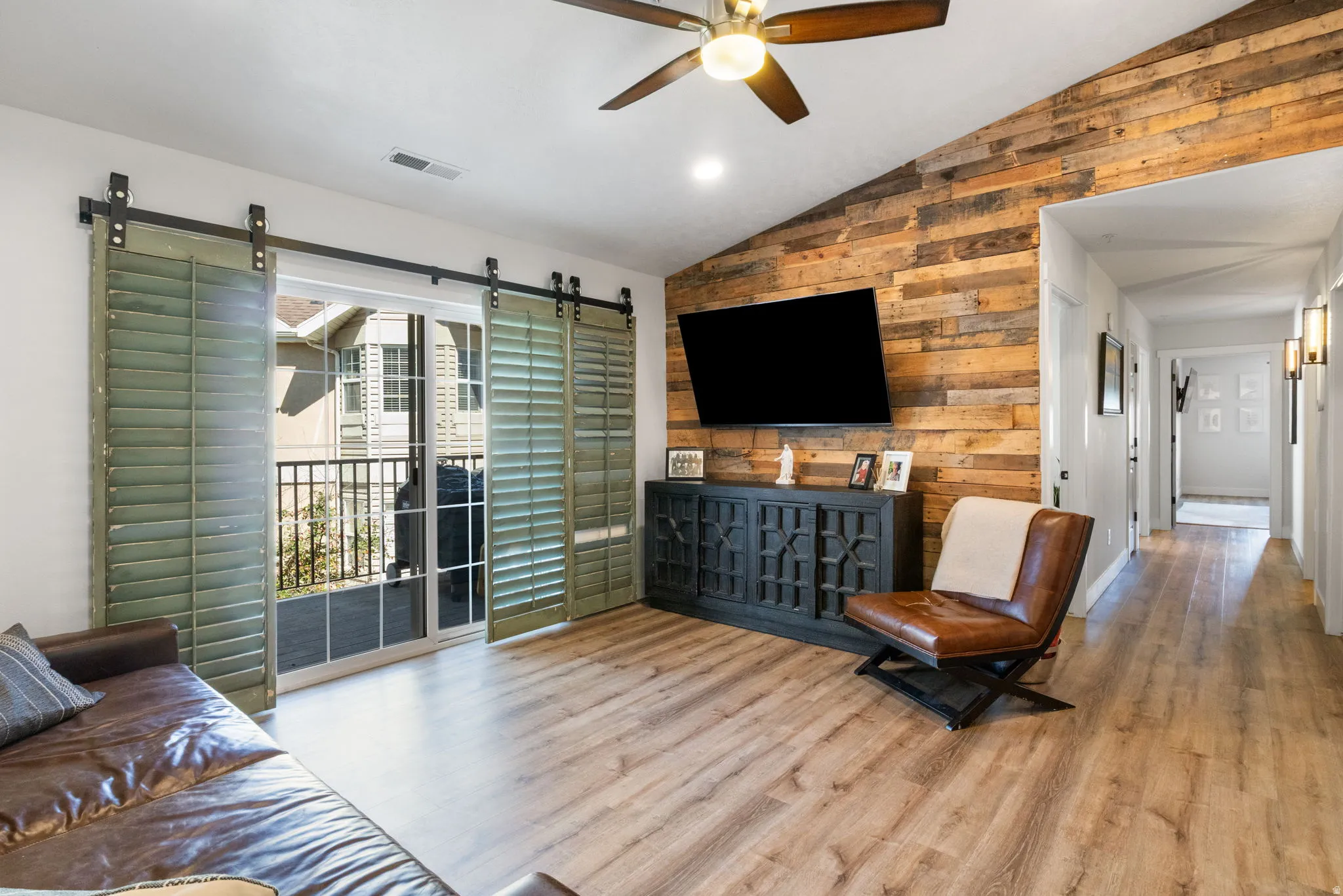 Living area featuring wood-finish flooring, a vaulted ceiling with a ceiling fan, and a reclaimed wood accent wall