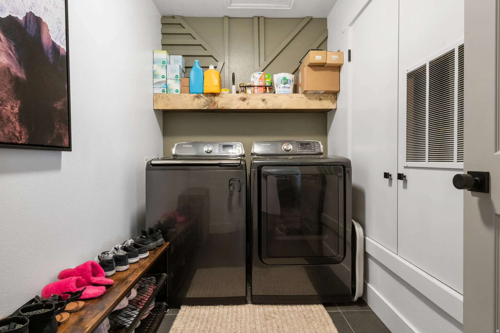 Dedicated laundry area featuring a wood-finish floating shelf, a decorative wood-panel accent wall, and a built-in storage unit