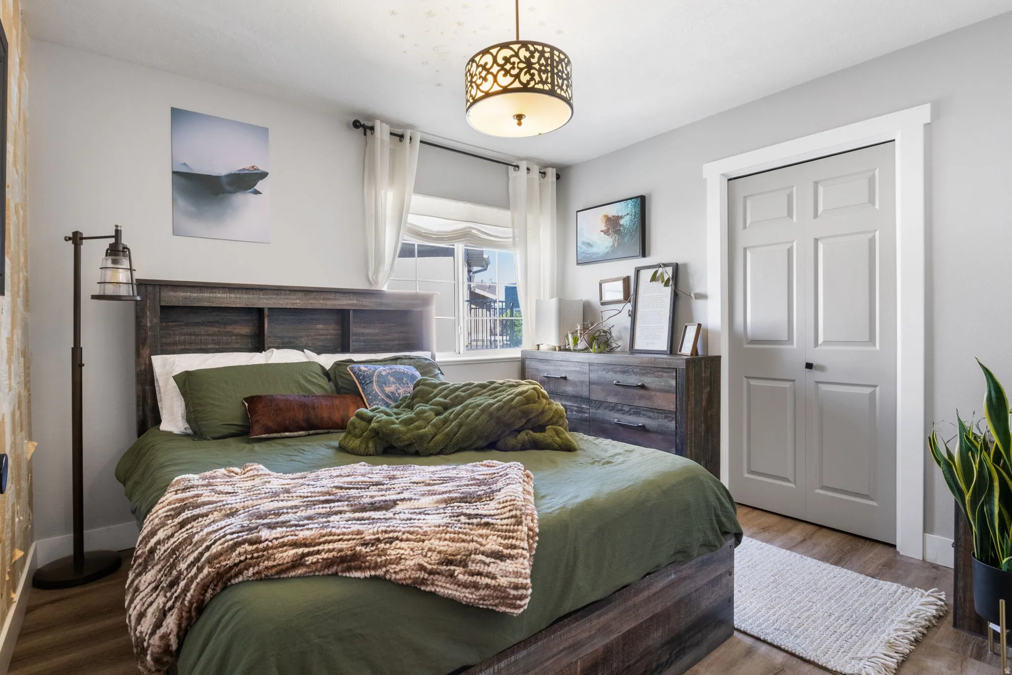 Spacious bedroom featuring wood-finish flooring, a contemporary ceiling light fixture, a paneled closet door, and a built-in headboard with storage compartments