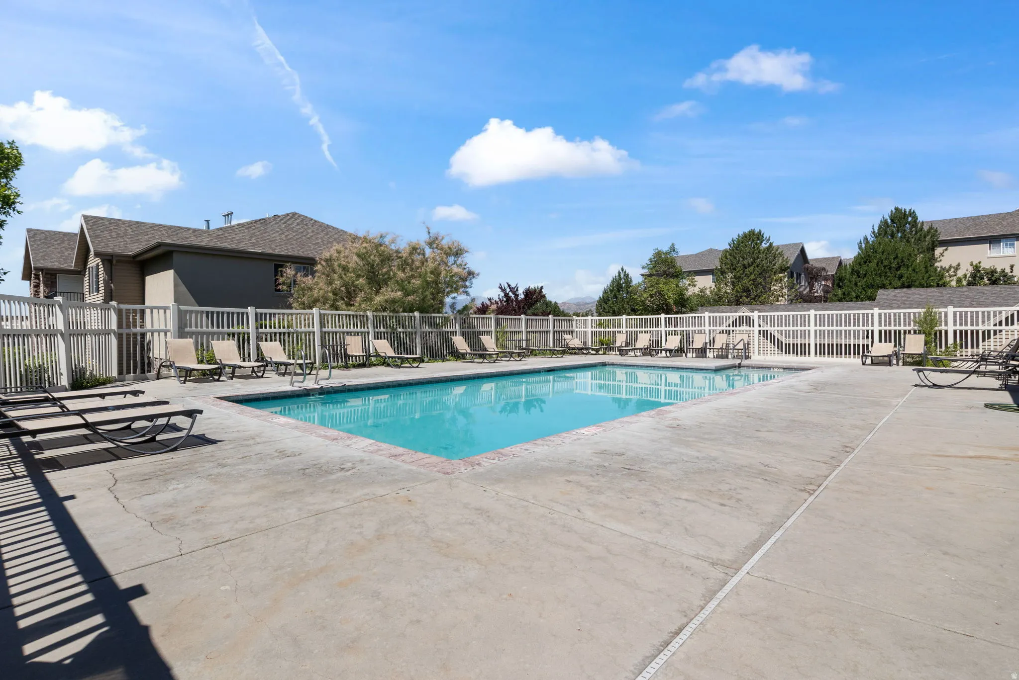 Rectangular swimming pool surrounded by a concrete deck and white fencing
