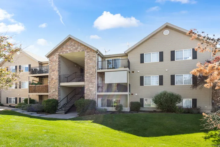 Multi-level residential building featuring stone veneer accents, tan siding, and multiple balconies