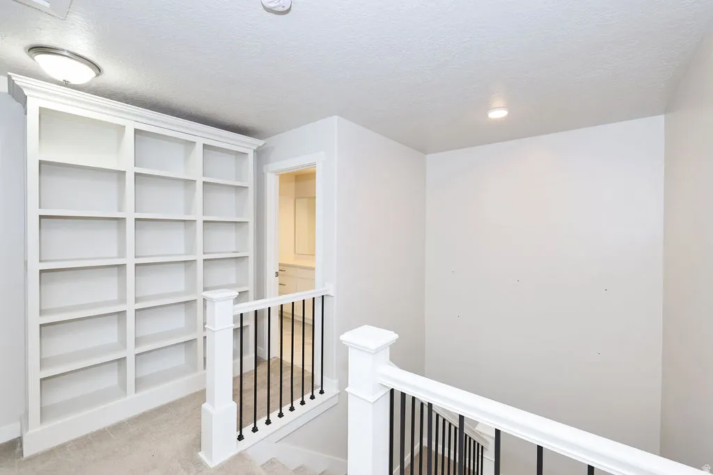 Built-in custom shelving, white painted wood newel posts, black iron balusters, recessed ceiling lighting, and a drum ceiling light fixture