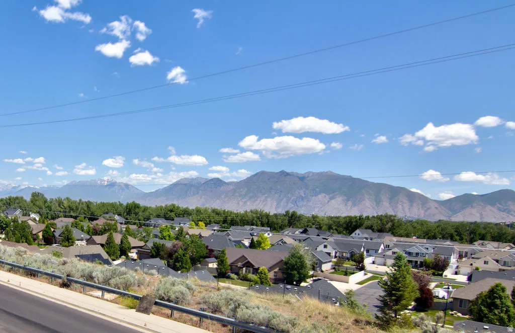 Neighborhood setting with residential rooftops and mature trees, backed by distant mountains under a blue sky with scattered clouds
