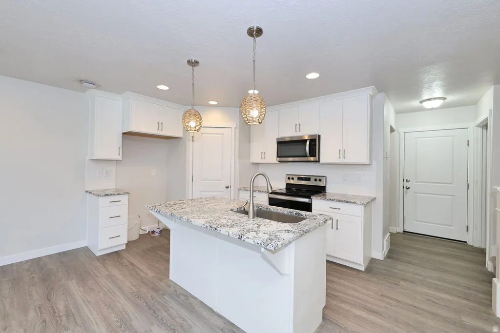 Contemporary kitchen featuring an island with an undermount sink, white cabinetry, granite-finish countertops, stainless steel appliances, and wood-finish flooring