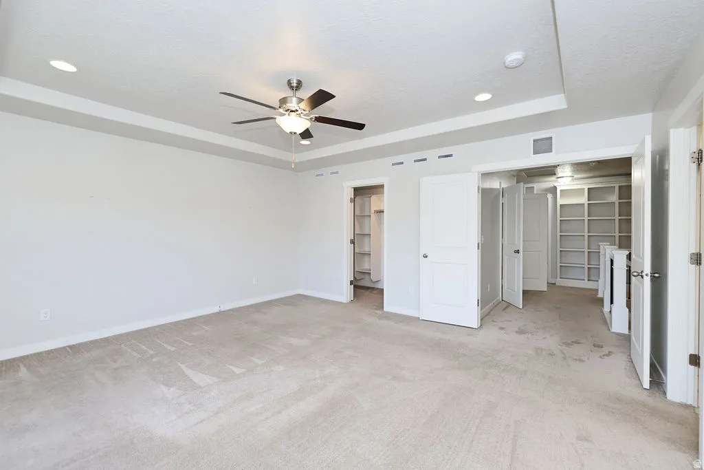 Spacious room featuring neutral carpeting, a tray ceiling with recessed lighting, and a ceiling fan with light fixture
