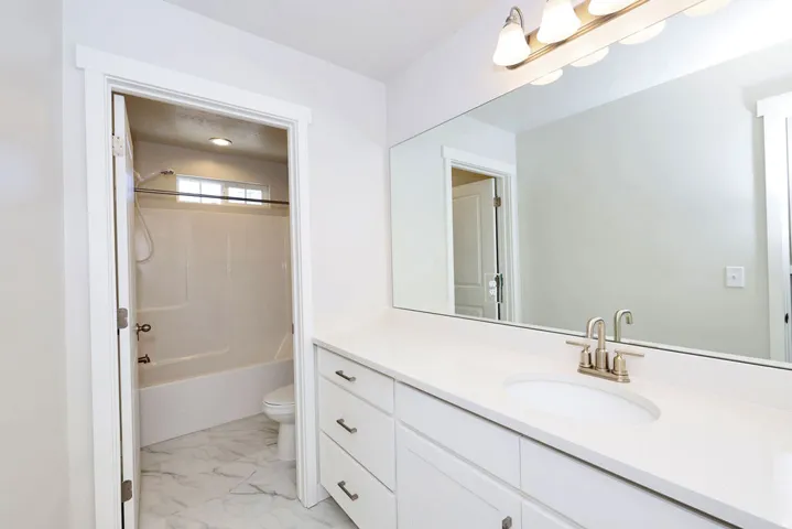 Bathroom vanity featuring a single undermount sink, brushed nickel faucet, light-toned countertop, and recessed panel cabinetry