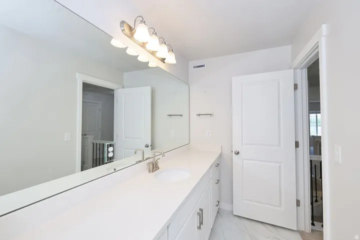 Vanity area featuring a wide mirror, a six-light vanity fixture, a white countertop with an integrated sink, brushed nickel faucet, and white shaker-style cabinetry with brushed nickel hardware