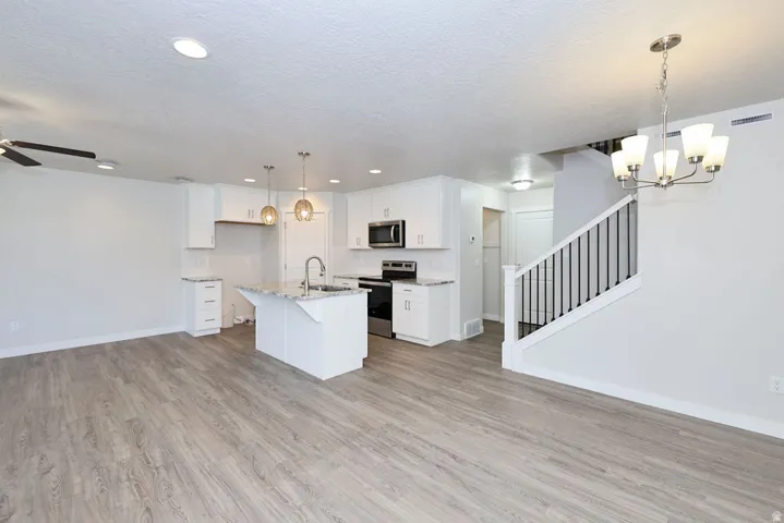 Contemporary open-concept living space featuring wood-finish flooring, a modern kitchen island with an undermount sink, stainless steel appliances, and white cabinetry