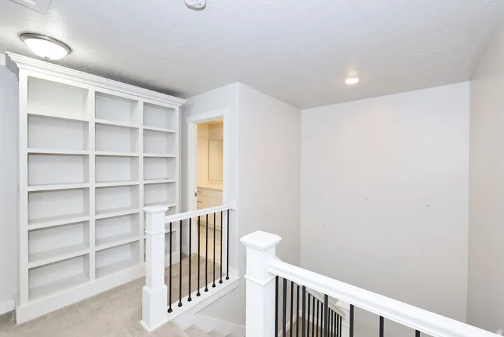 Built-in custom shelving, white painted wood newel posts, black iron balusters, recessed ceiling lighting, and a drum ceiling light fixture