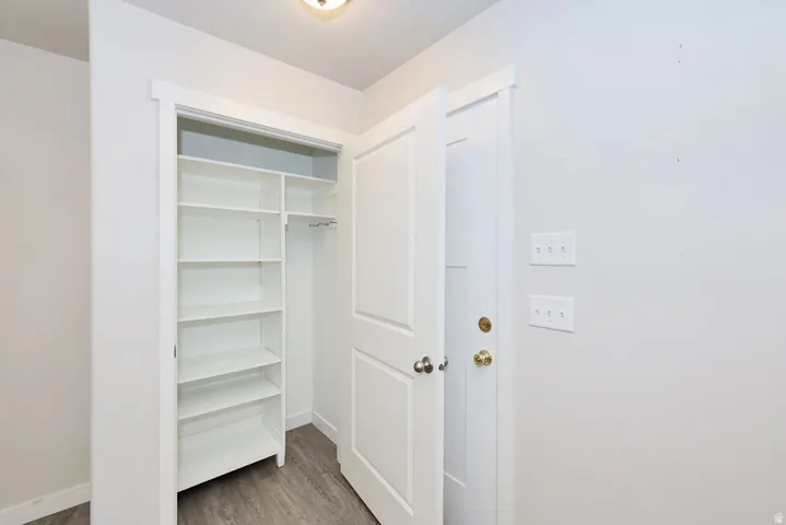 Built-in shelving and hanging rod storage, wood-finish flooring, white trim, white interior doors, and overhead lighting fixture