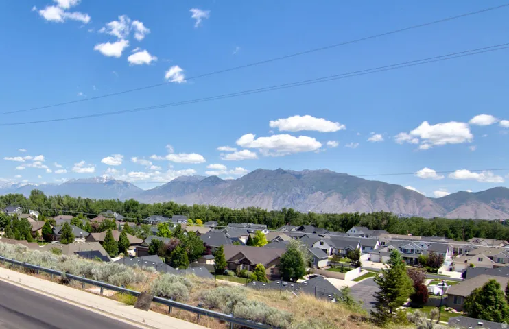 Neighborhood setting with residential rooftops and mature trees, backed by distant mountains under a blue sky with scattered clouds