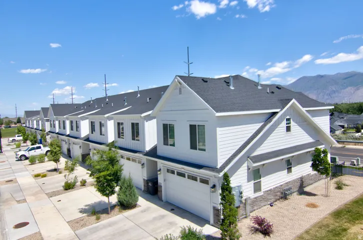 Modern townhome row featuring white horizontal siding, dark shingle roofing, and attached garages