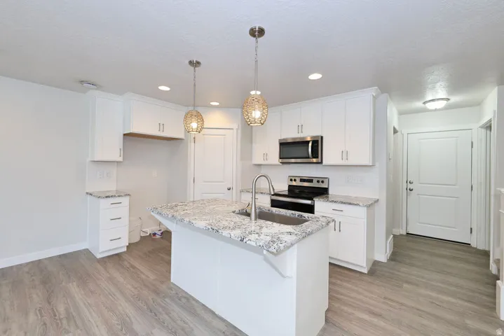 Contemporary kitchen featuring an island with an undermount sink, white cabinetry, granite-finish countertops, stainless steel appliances, and wood-finish flooring