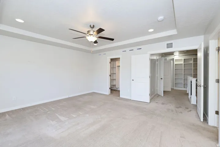 Spacious room featuring neutral carpeting, a tray ceiling with recessed lighting, and a ceiling fan with light fixture