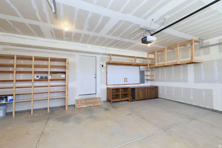 Spacious garage featuring extensive built-in wooden shelving, overhead storage racks, a utility door with steps, and a concrete floor