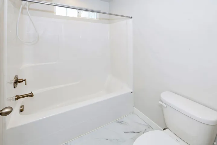 White bathtub-shower combination featuring a bronzed fixture set, a handheld shower head, and a privacy window