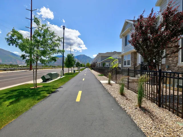 Paved pathway with central yellow stripe bordered by manicured grass and ornamental trees