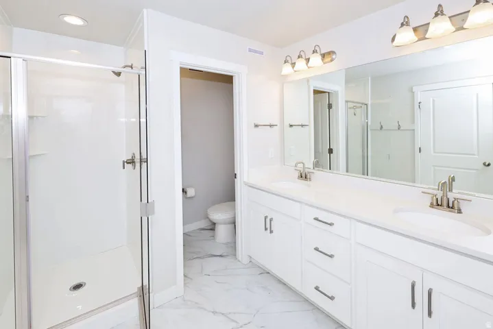 Bathroom featuring a glass-enclosed shower, dual vanity with white cabinetry, light-toned countertops, and a large wall-mounted mirror