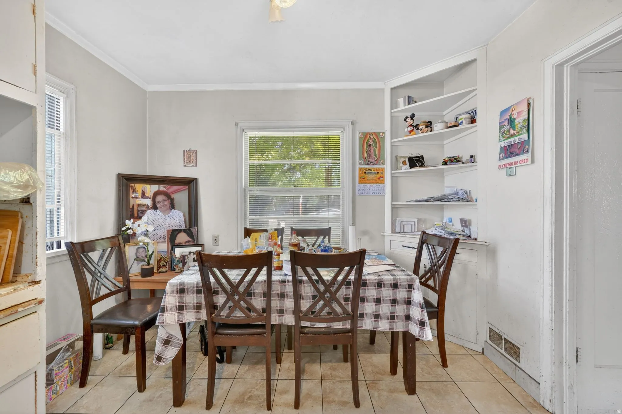 Dining area featuring tile flooring, dual windows with blinds, a corner built-in shelving unit with lower cabinetry, and crown molding