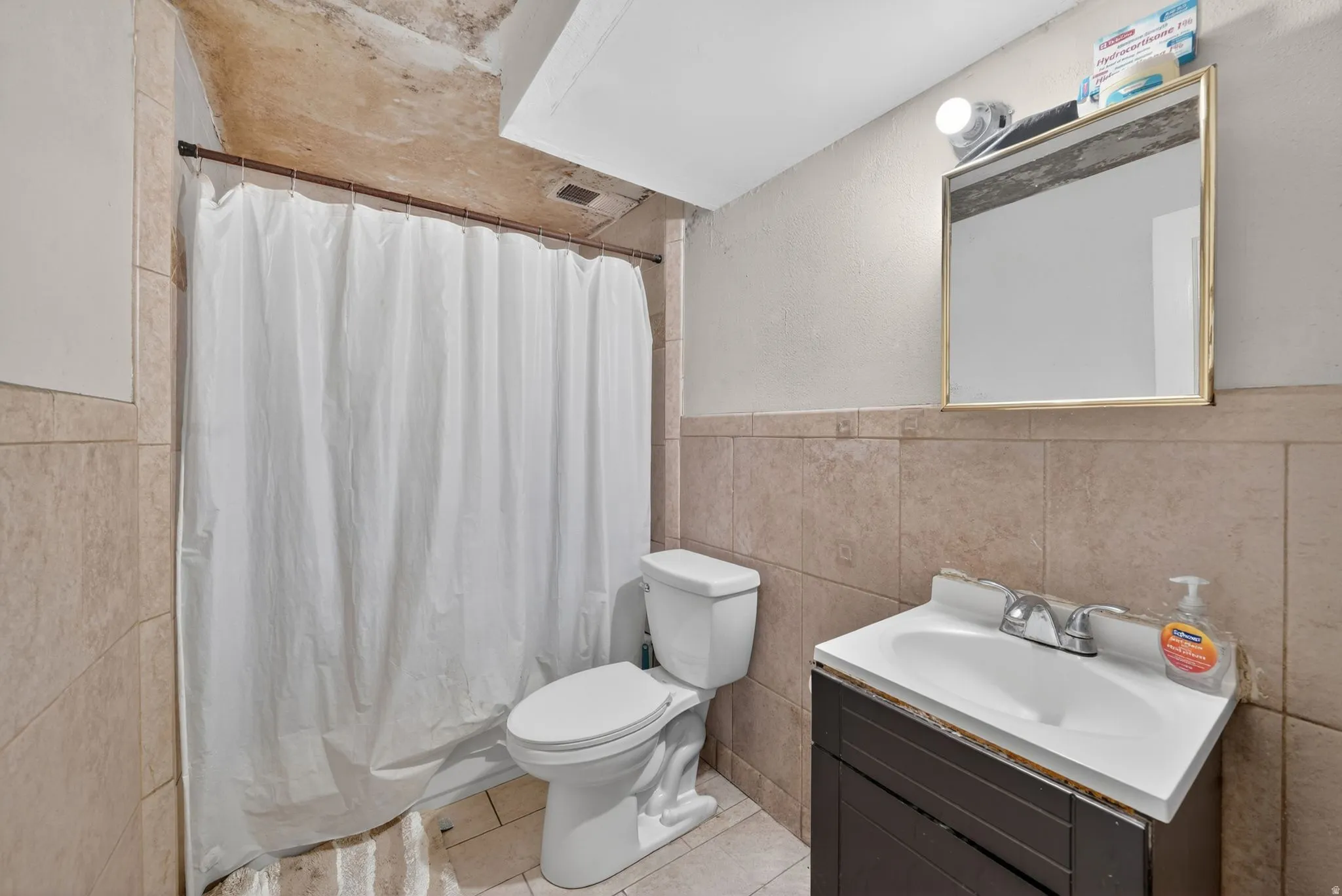 Bathroom featuring full-height tiled walls, a vanity with integrated sink, and a framed mirror with overhead lighting