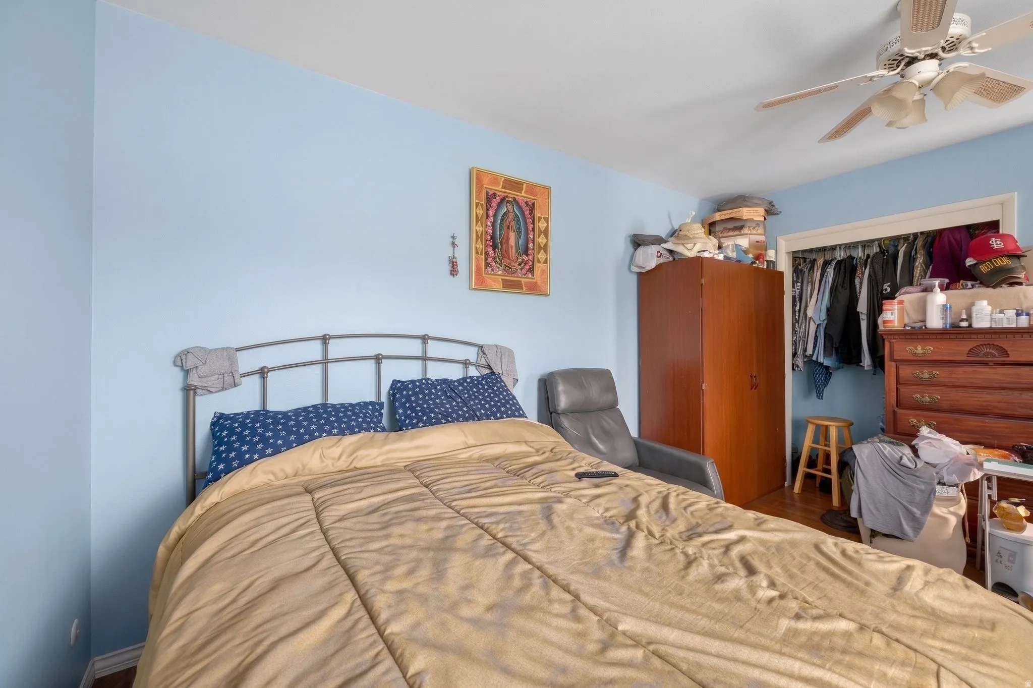 Bedroom featuring light blue walls, wood-finish flooring, a ceiling fan, and a built-in closet with an open doorway