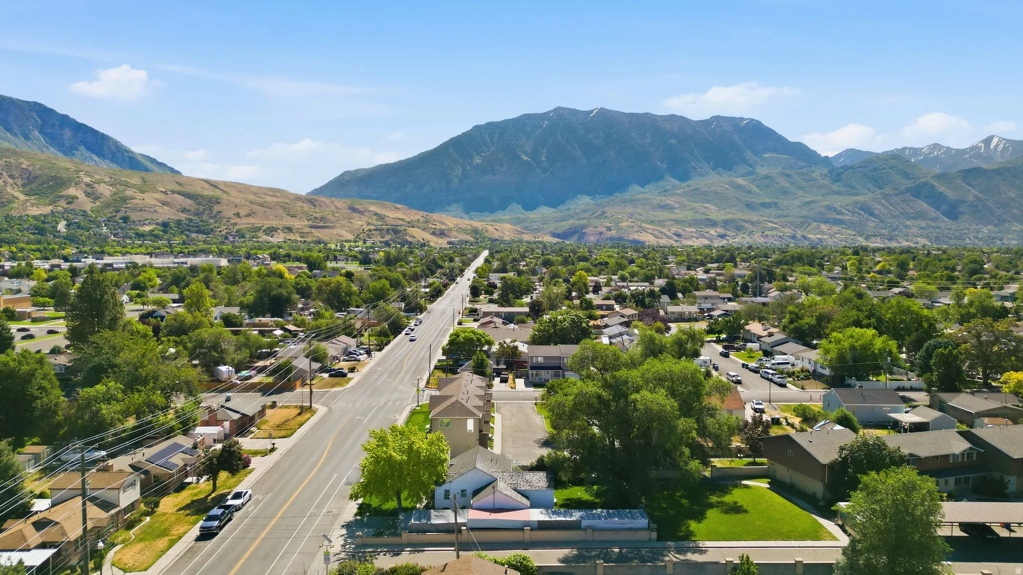 Expansive neighborhood with mature trees, a prominent paved road, and distant mountains