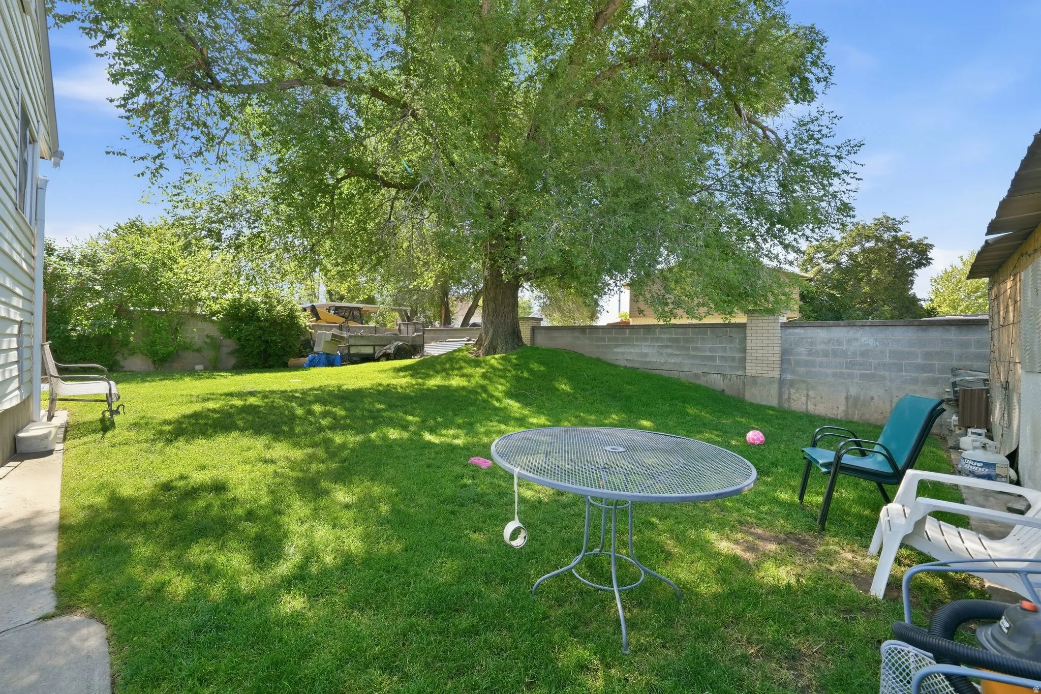 Expansive green lawn featuring a mature shade tree, concrete block retaining wall, and a sloped landscape