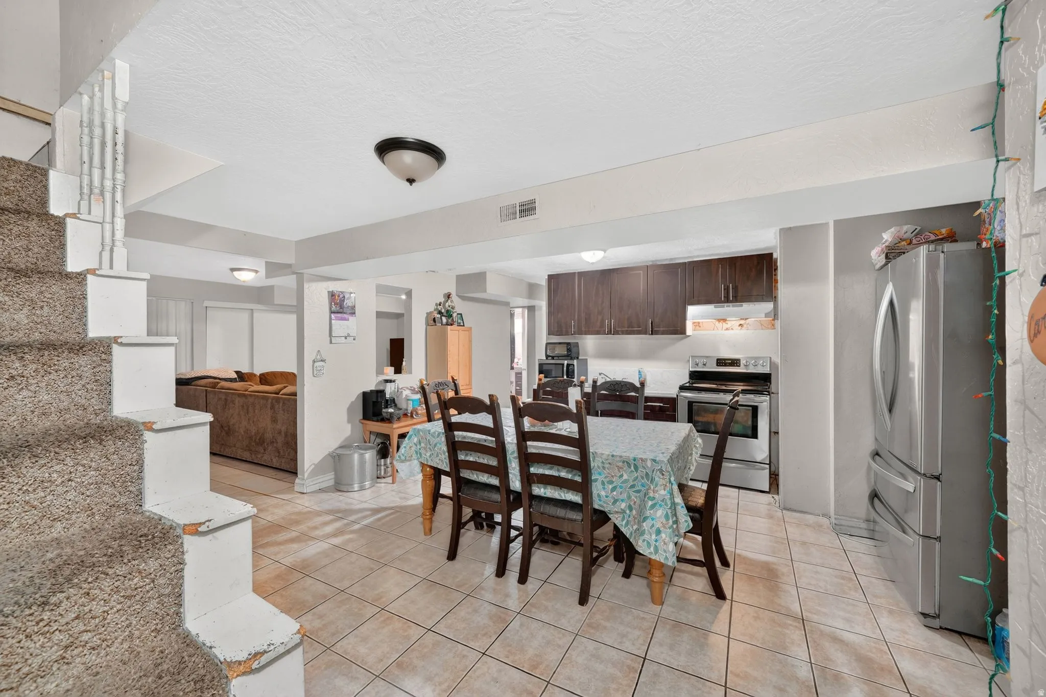 Kitchen and dining area featuring tile flooring, dark wood cabinetry, a stainless steel refrigerator, and a stainless steel range with overhead microwave
