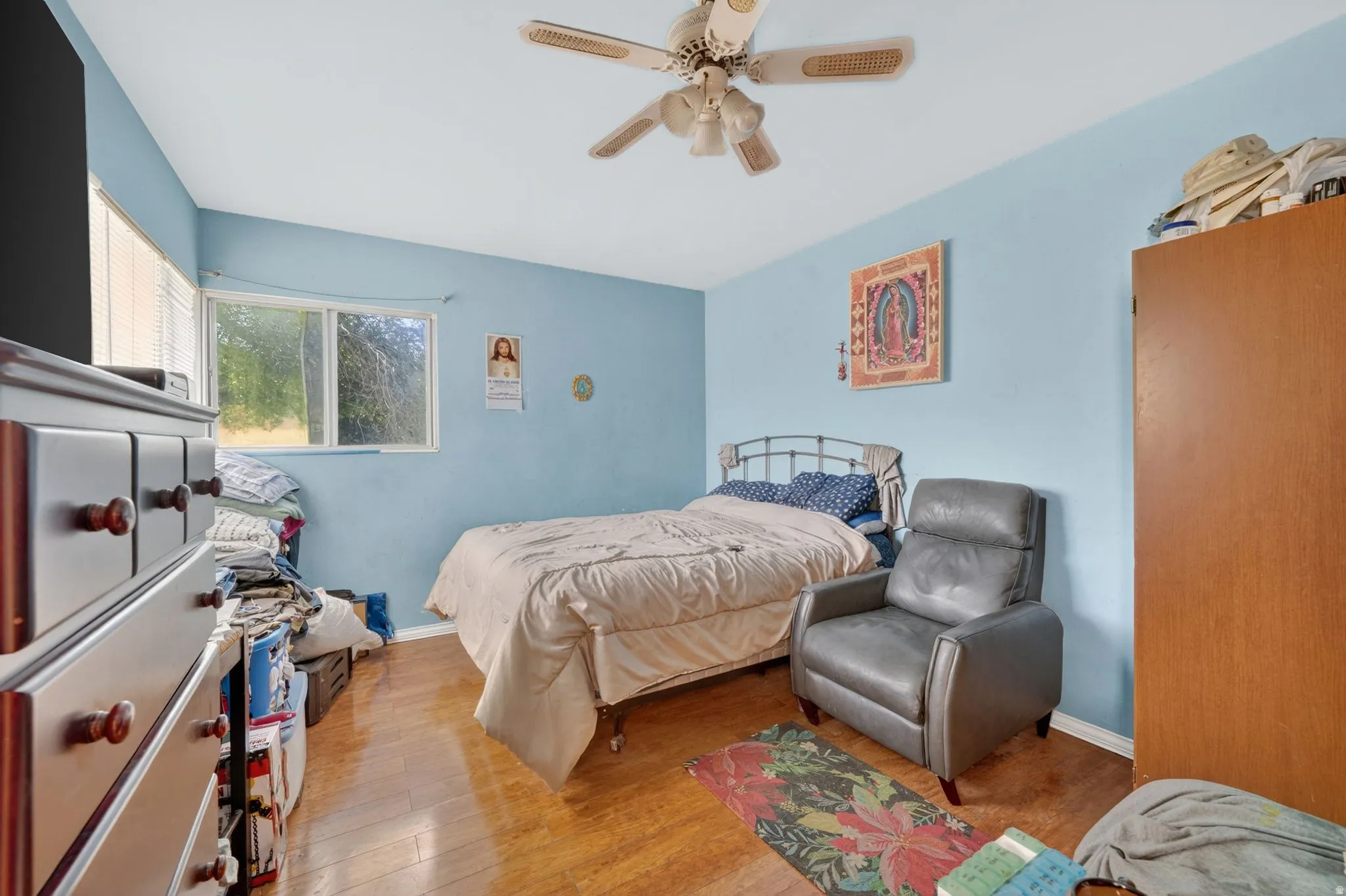 Bedroom featuring a ceiling fan, wood-finish flooring, a window with horizontal blinds, and light blue walls