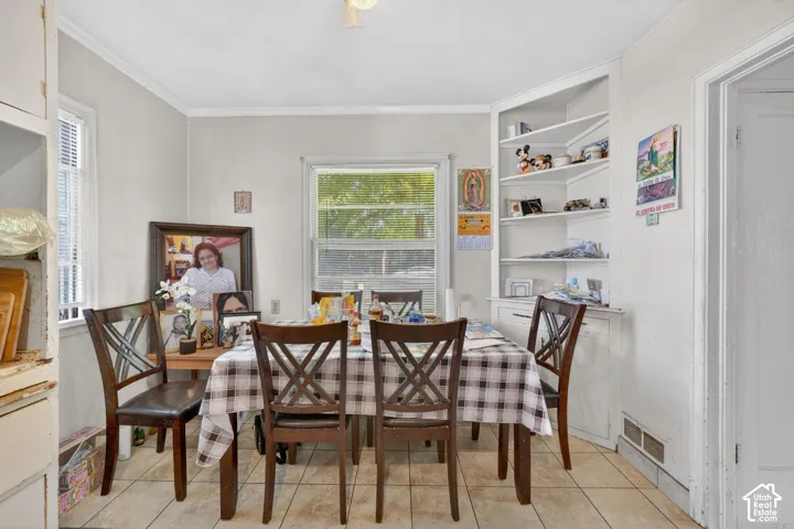 Dining area featuring tile flooring, dual windows with blinds, a corner built-in shelving unit with lower cabinetry, and crown molding