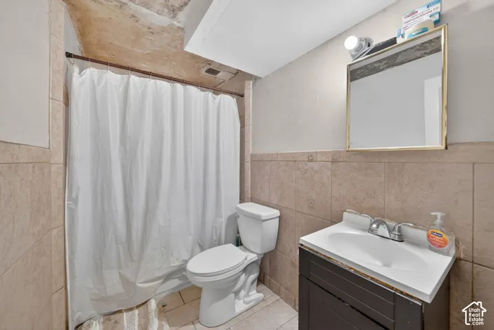 Bathroom featuring full-height tiled walls, a vanity with integrated sink, and a framed mirror with overhead lighting