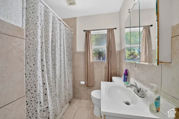 Bathroom featuring tiled walls, a window with natural light, a white vanity with an integrated sink, a mirrored medicine cabinet, and tiled flooring