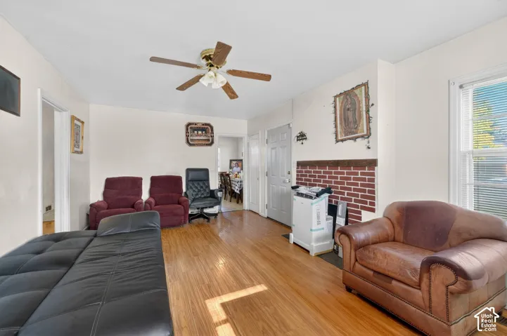 Spacious living area featuring wood-finish flooring, light neutral wall paint, and a ceiling fan