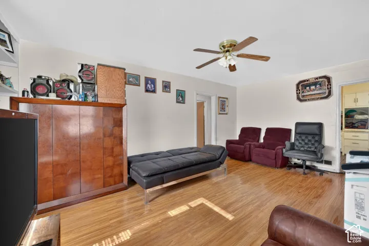 Bright interior room featuring wood-finish flooring, a ceiling fan with integrated lighting, and neutral wall tones