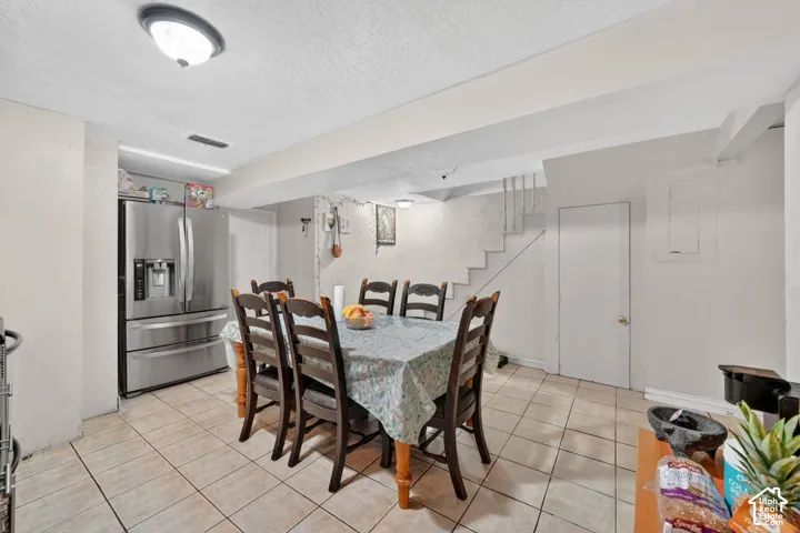 Spacious dining area featuring neutral-toned tile flooring, a built-in stainless steel refrigerator, and a staircase with a white railing