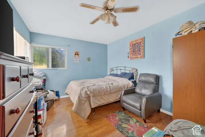 Bedroom featuring a ceiling fan, wood-finish flooring, a window with horizontal blinds, and light blue walls