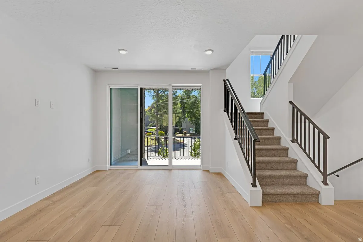 Open concept living space featuring wood-finish flooring, a contemporary staircase with metal railings, and a sliding glass door opening to an outdoor balcony