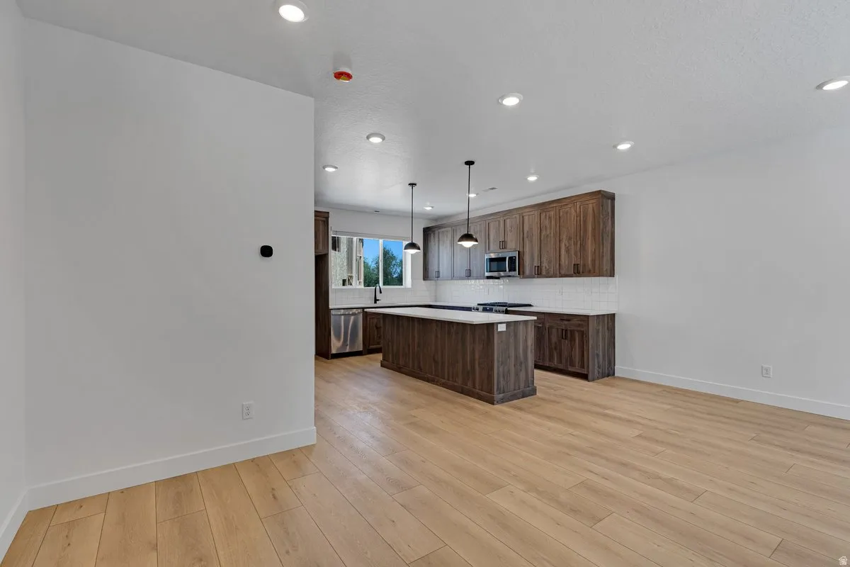Open-concept kitchen featuring wood-finish cabinetry, a large island with a light-toned countertop, stainless steel appliances, and wood-finish flooring