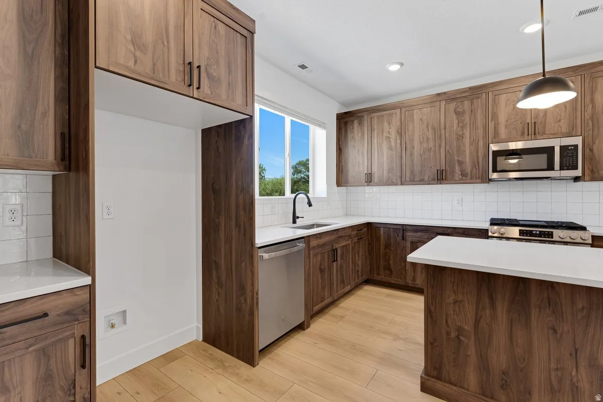 Kitchen featuring wood-grain cabinetry, stainless steel appliances, a white subway tile backsplash, and light-toned wood-finish flooring