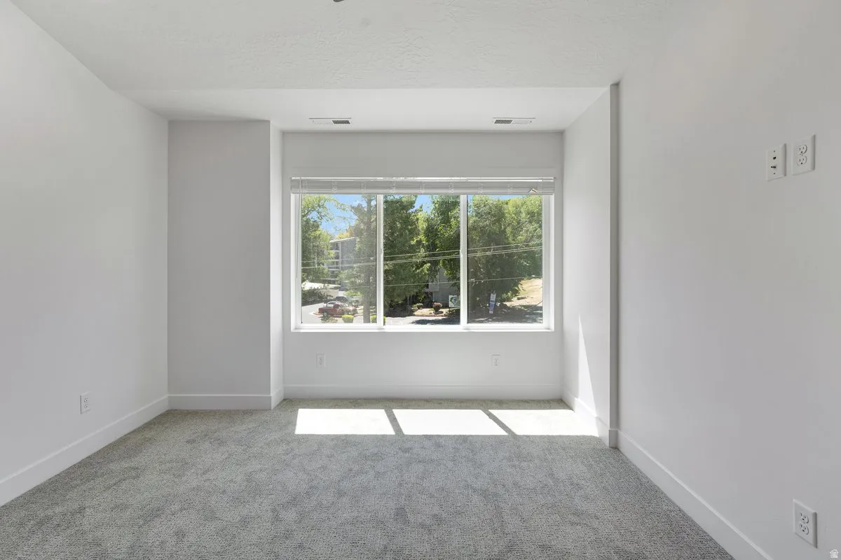 Bright interior space featuring a large window with white blinds, light gray carpet, white walls, and white baseboards