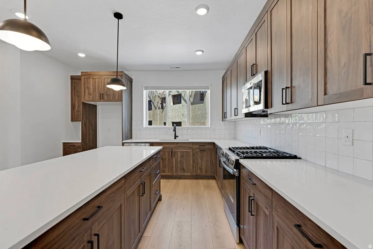 Kitchen featuring an expansive island with white countertops, wood-finish cabinetry, stainless steel appliances, a gas range, and a white subway tile backsplash