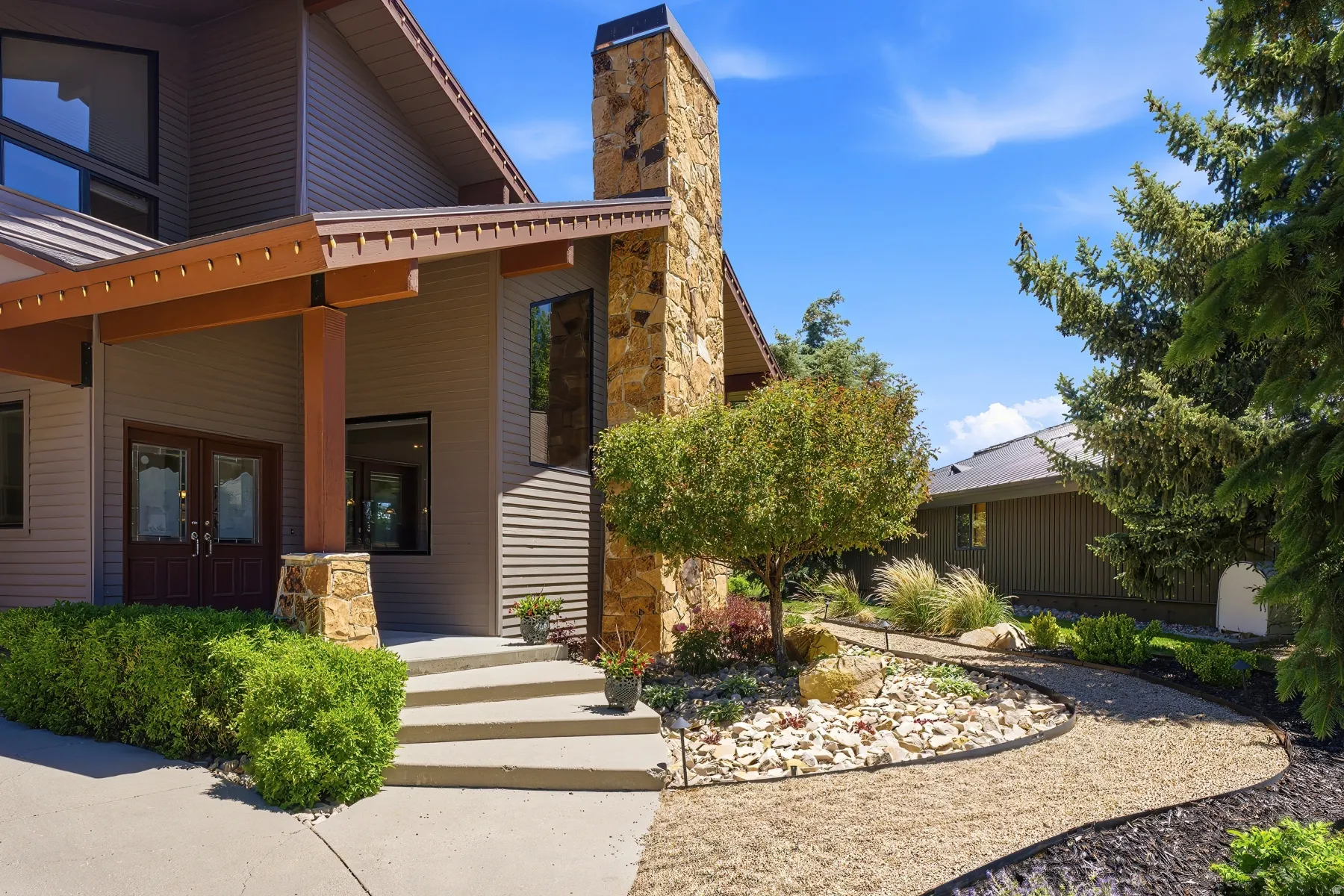 Modern exterior featuring a stone chimney, wood beams, and double entry doors