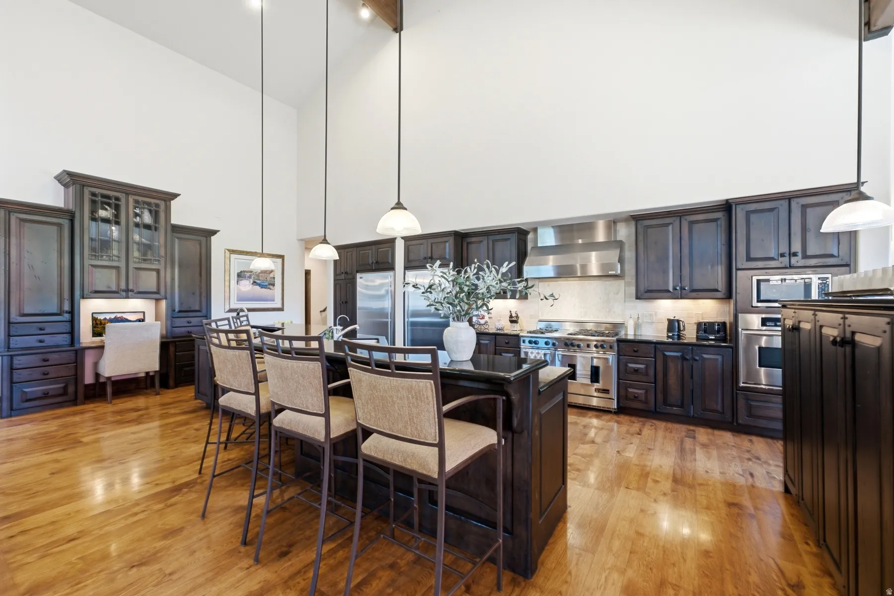 Vaulted ceilings enhance this kitchen featuring hardwood flooring, dark wood cabinetry, a central island with bar seating, and stainless steel appliances