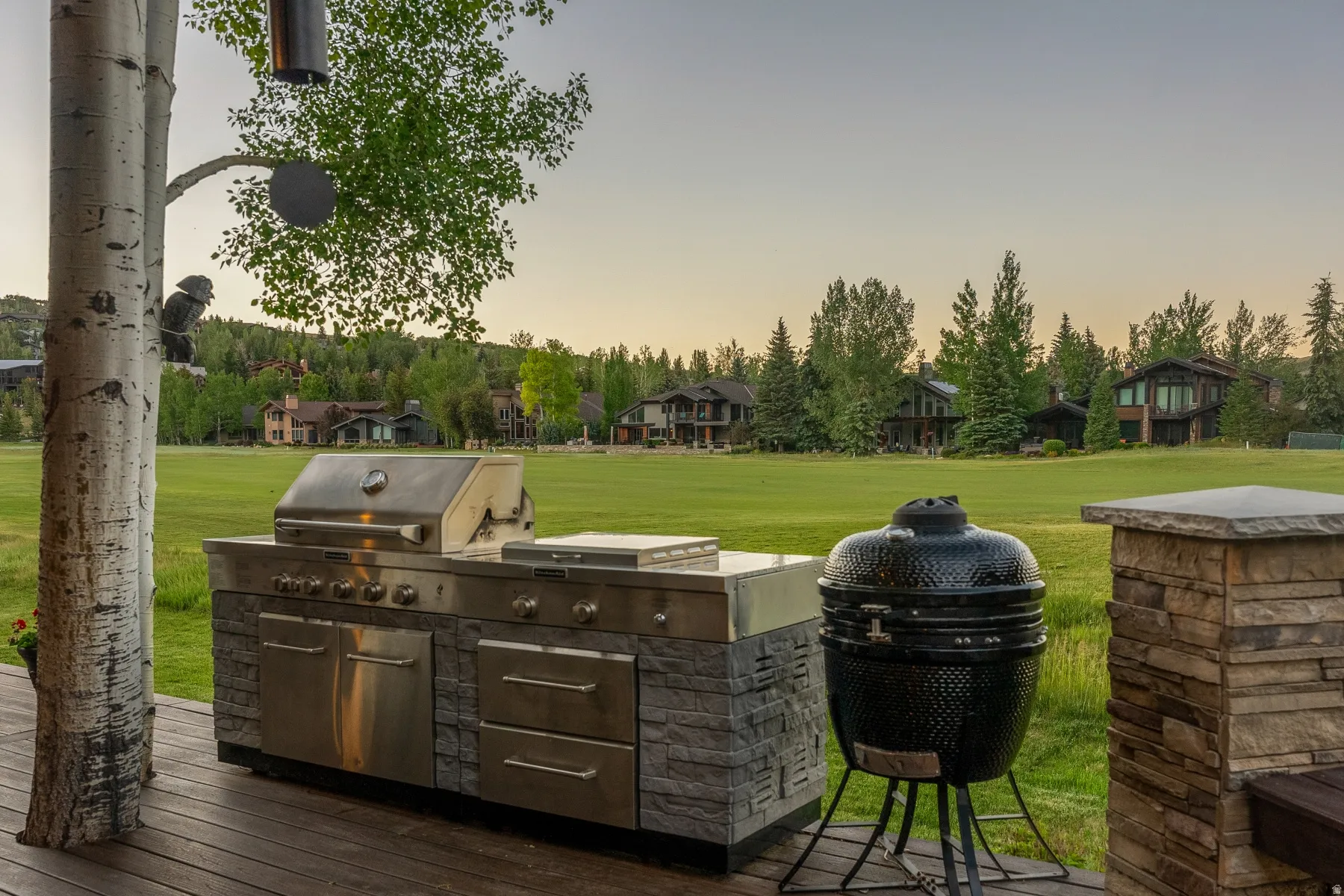 Outdoor cooking station featuring a stainless steel built-in grill, stone-clad base, and a separate ceramic smoker