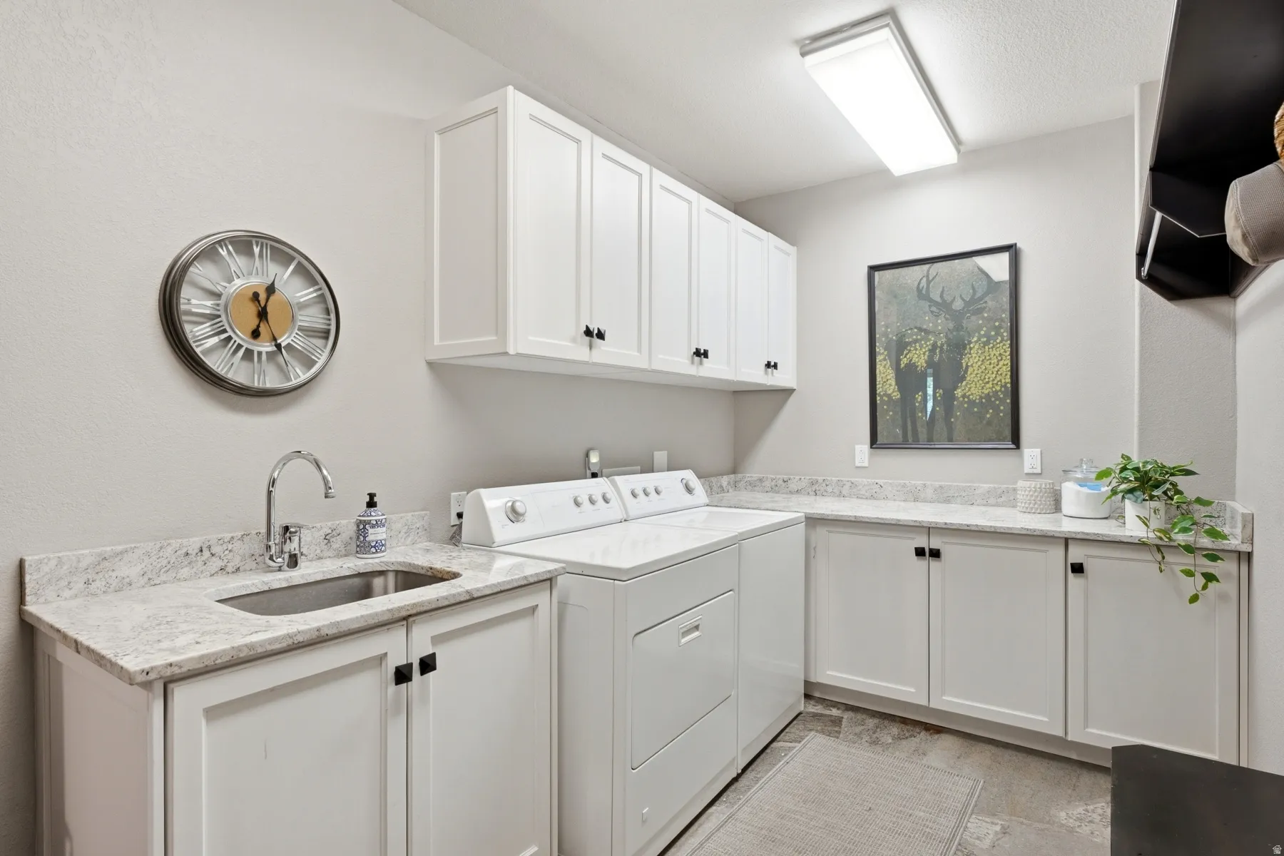 Laundry room with extensive white cabinetry, light-toned countertops, and a utility sink with a chrome faucet