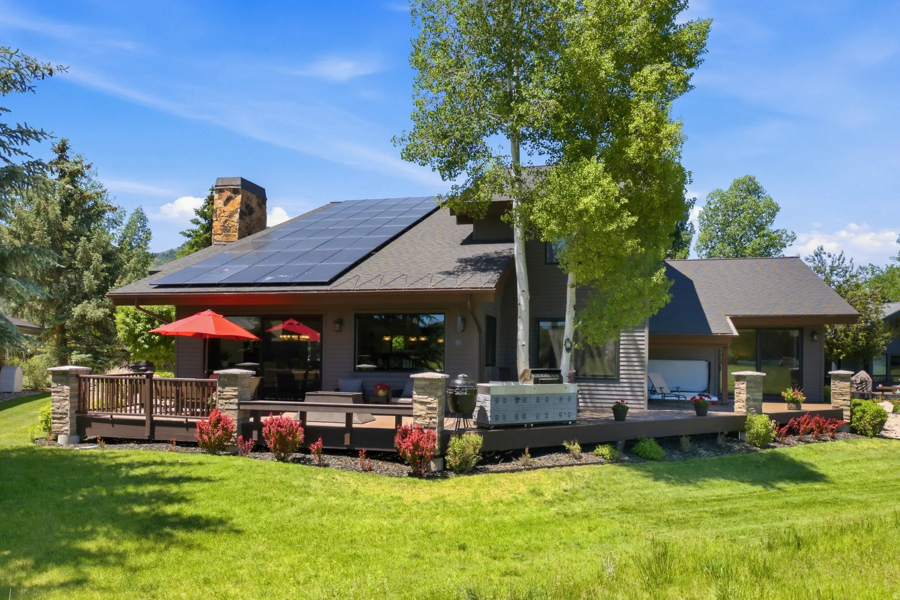 Contemporary residence featuring a spacious multi-level rear deck, integrated solar panels, a stone chimney, and expansive windows